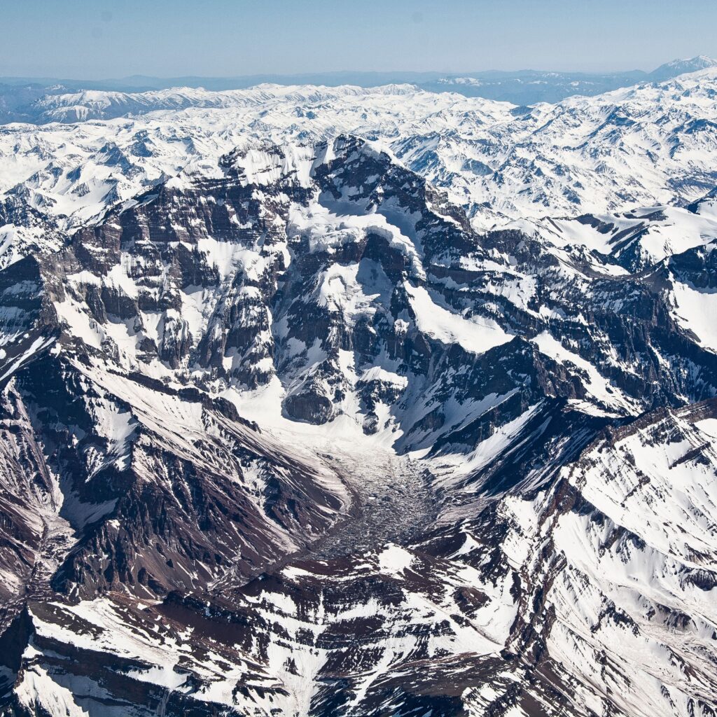 A stunning aerial view of Mount Aconcagua, the highest peak in the Andes mountain range, surrounded by dramatic ridges and vast, rugged terrain.