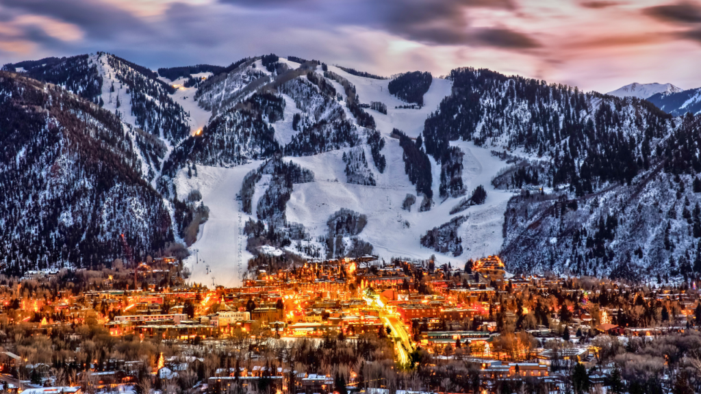 Lit-up ski slope at dusk, with lights illuminating the trail as skiers descend under the fading evening sky in a Colorado Ski Town