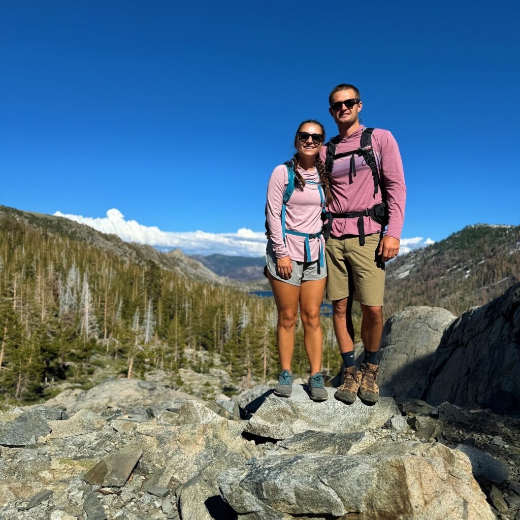 A couple hiking in national parks, enjoying a scenic trail surrounded by towering pines and crystal-clear waters.