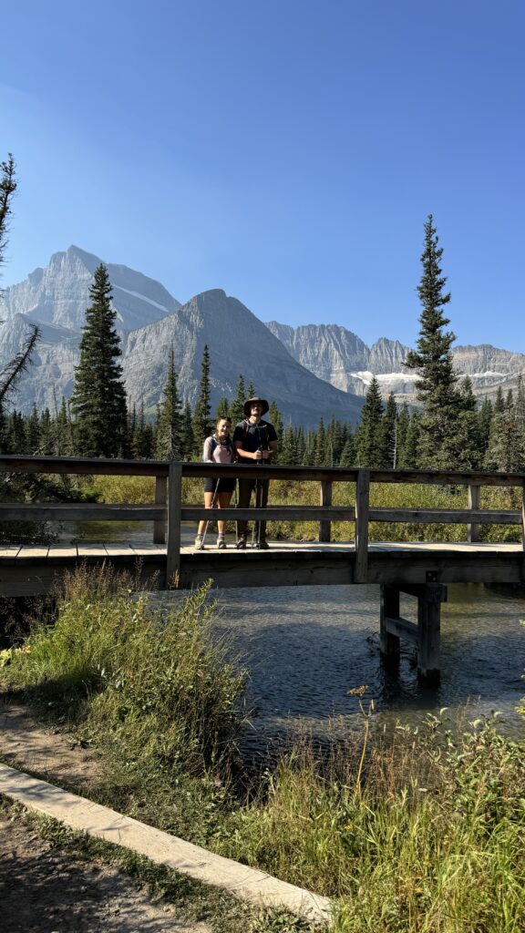 Couple posing on a scenic bridge surrounded by towering mountains and a serene lake in Glacier National Park, showcasing tips to avoid crowds at National Parks for a peaceful experience.