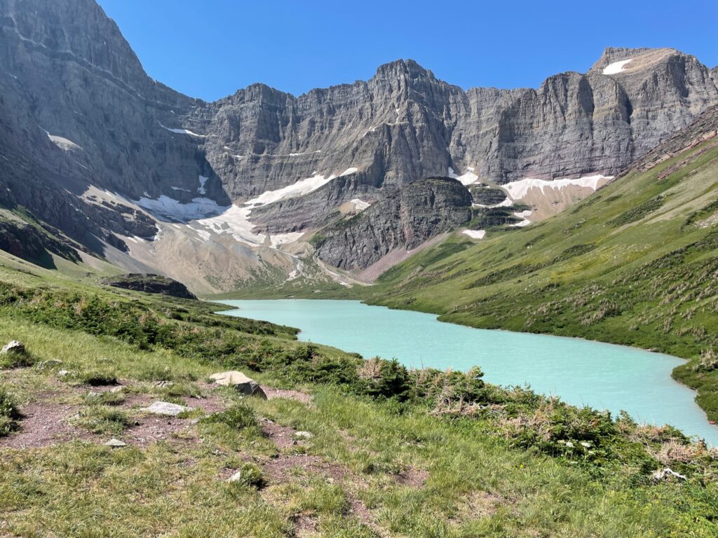 Scenic landscape of Cracker Lake in Glacier National Park, with vibrant turquoise waters surrounded by rugged mountains and lush greenery, showcasing the park's natural beauty.