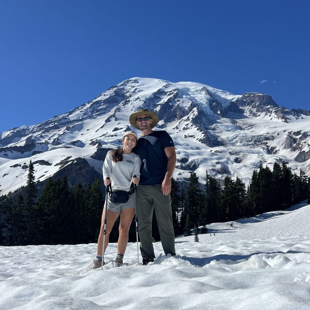 A couple posing during a hike with Mount Rainier in the background, showcasing the beauty of their National Park trip planning and adventure in the Pacific Northwest.
