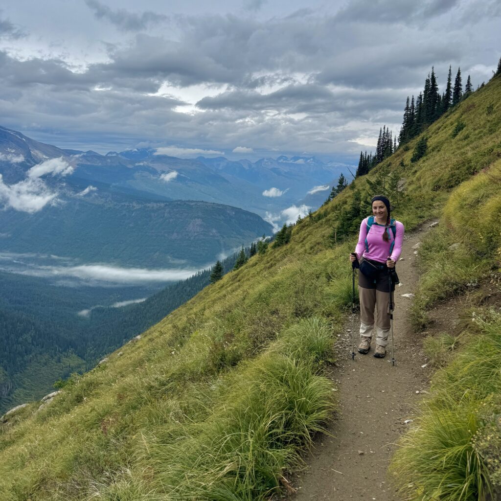 Hiker posing on the Highline Trail in Glacier National Park with dramatic mountain views in the background.