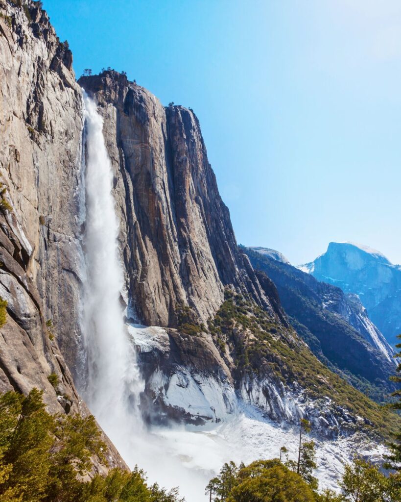 A scenic overlook of Yosemite’s majestic waterfalls surrounded by lush greenery and towering granite peaks, visible from a popular Yosemite hike.