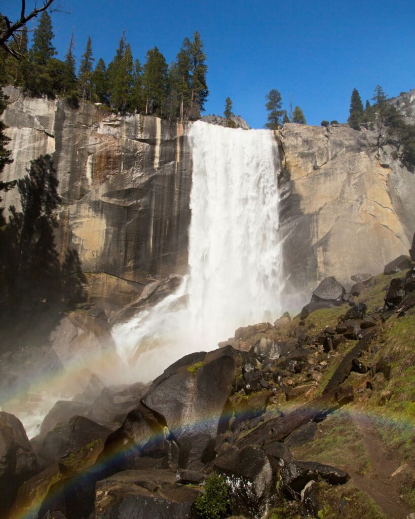 A stunning view of Nevada Fall in Yosemite, with a rainbow arching over the waterfall, captured from a scenic viewpoint along a Yosemite hike.