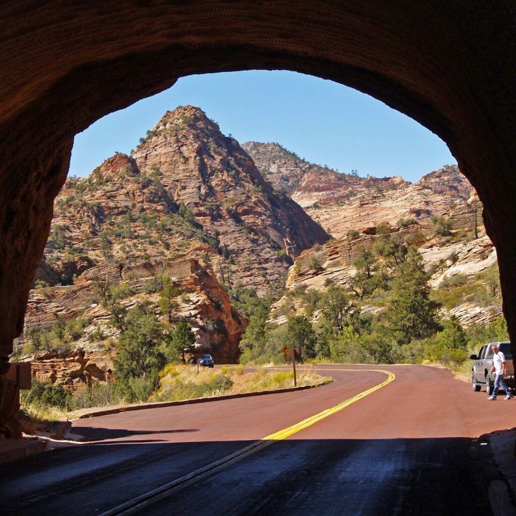 Scenic drive through Zion National Park, showcasing the winding road leading into a dramatic tunnel carved into red rock cliffs, a highlight of this Zion National Park travel guide.