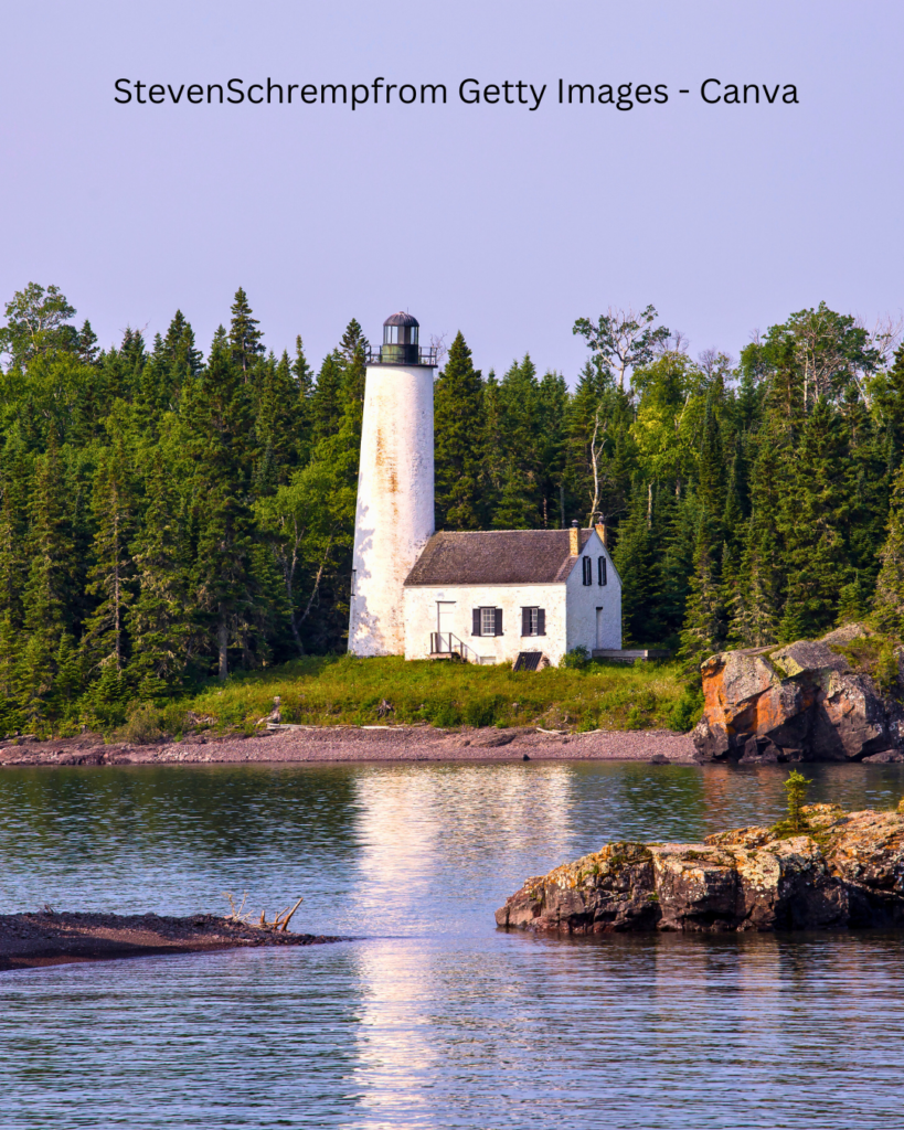The historic Rock Harbor Lighthouse standing tall against a blue sky, with its white tower and black lantern room overlooking the waters of Lake Superior.