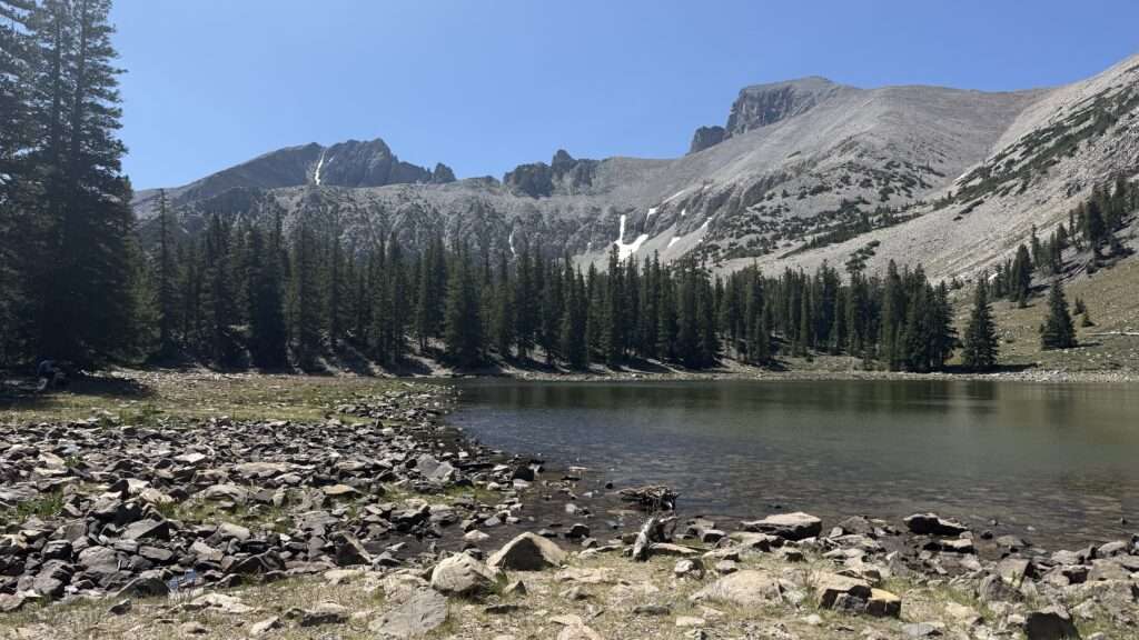 Stella Lake reflecting the craggy slopes of Wheeler Peak, surrounded by evergreens and high-alpine wilderness in Great Basin National Park.